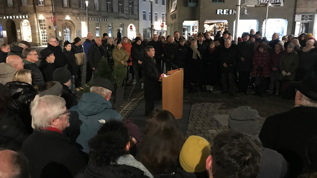 Ein Mann steht am Rednerpult. Außenherum stehen Menschen. und hören zu. | Bild: BR/Markus Feulner Ein Mann steht am Rednerpult. Außenherum stehen Menschen. und hören zu.