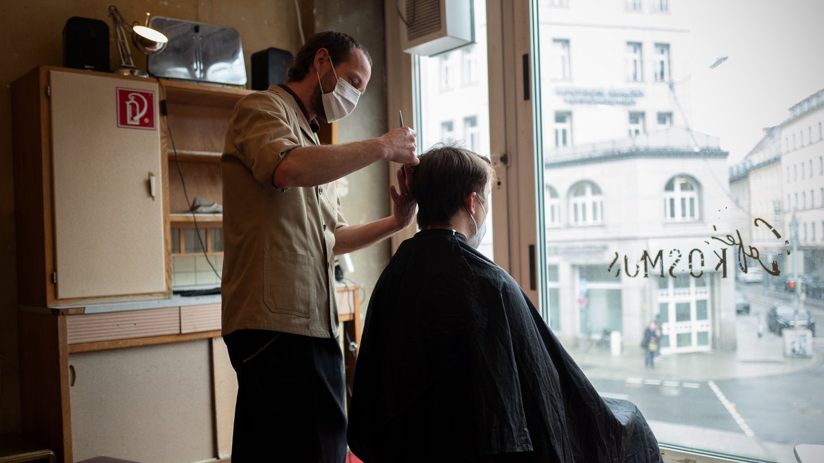 Der Inhaber des Café Kosmos schneidet einem Kunden die Haare. 