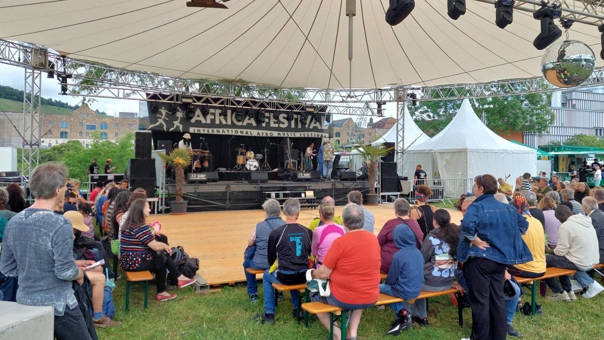 Eine Bühne beim Africa Festival in Würzburg, Zuschauerinnen und Zuschauer sitzen auf Bänken davor.