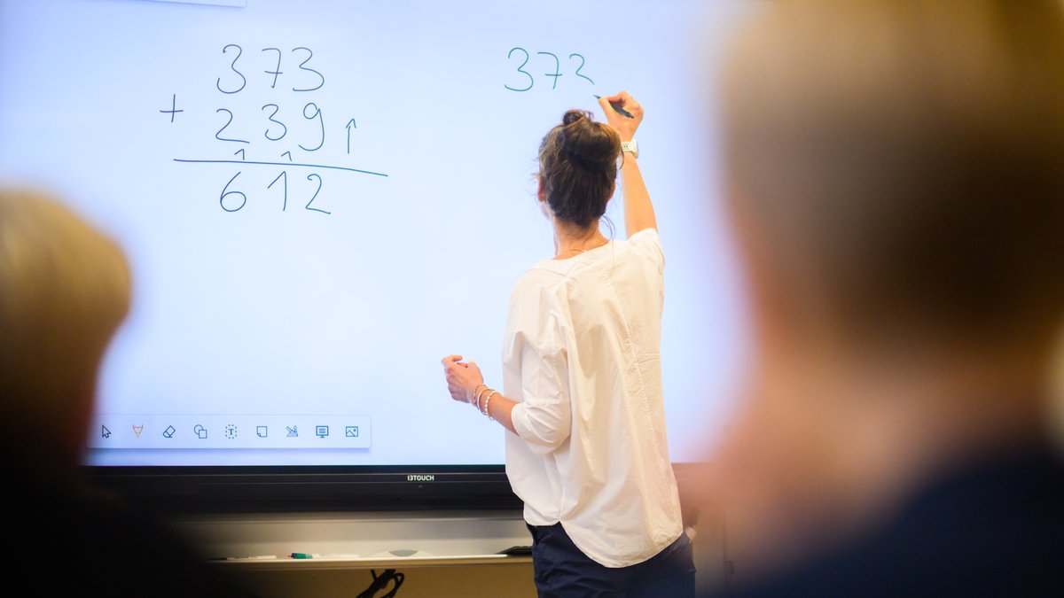 Lehrerin schreibt eine Mathematikaufgabe auf eine digitale Schultafel.