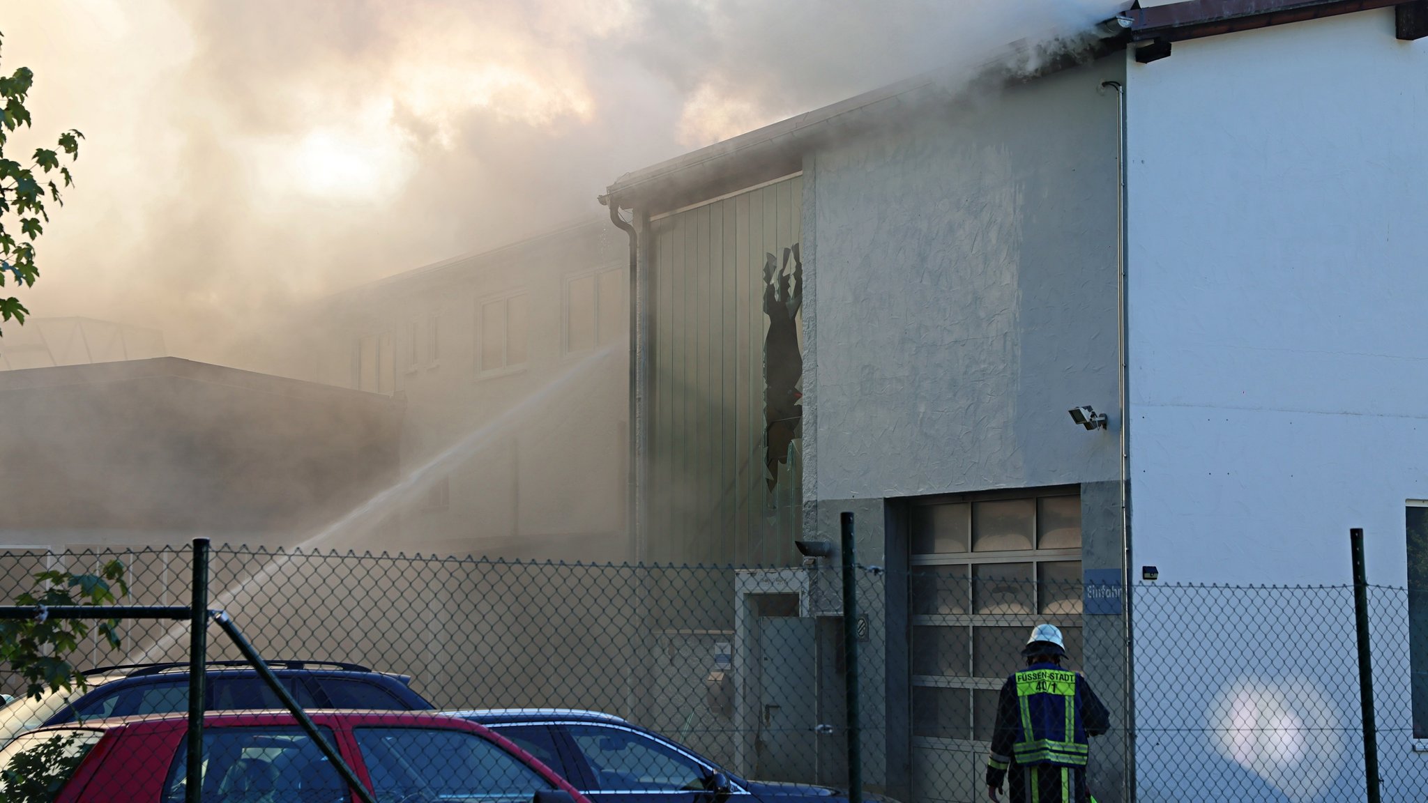 Eine große Halle ist in dichte Rauchschwaden gehüllt, ein Feuerwehrmann steht davor. | Bild: Pöppel/new-facts.eu Eine große Halle ist in dichte Rauchschwaden gehüllt, ein Feuerwehrmann steht davor.