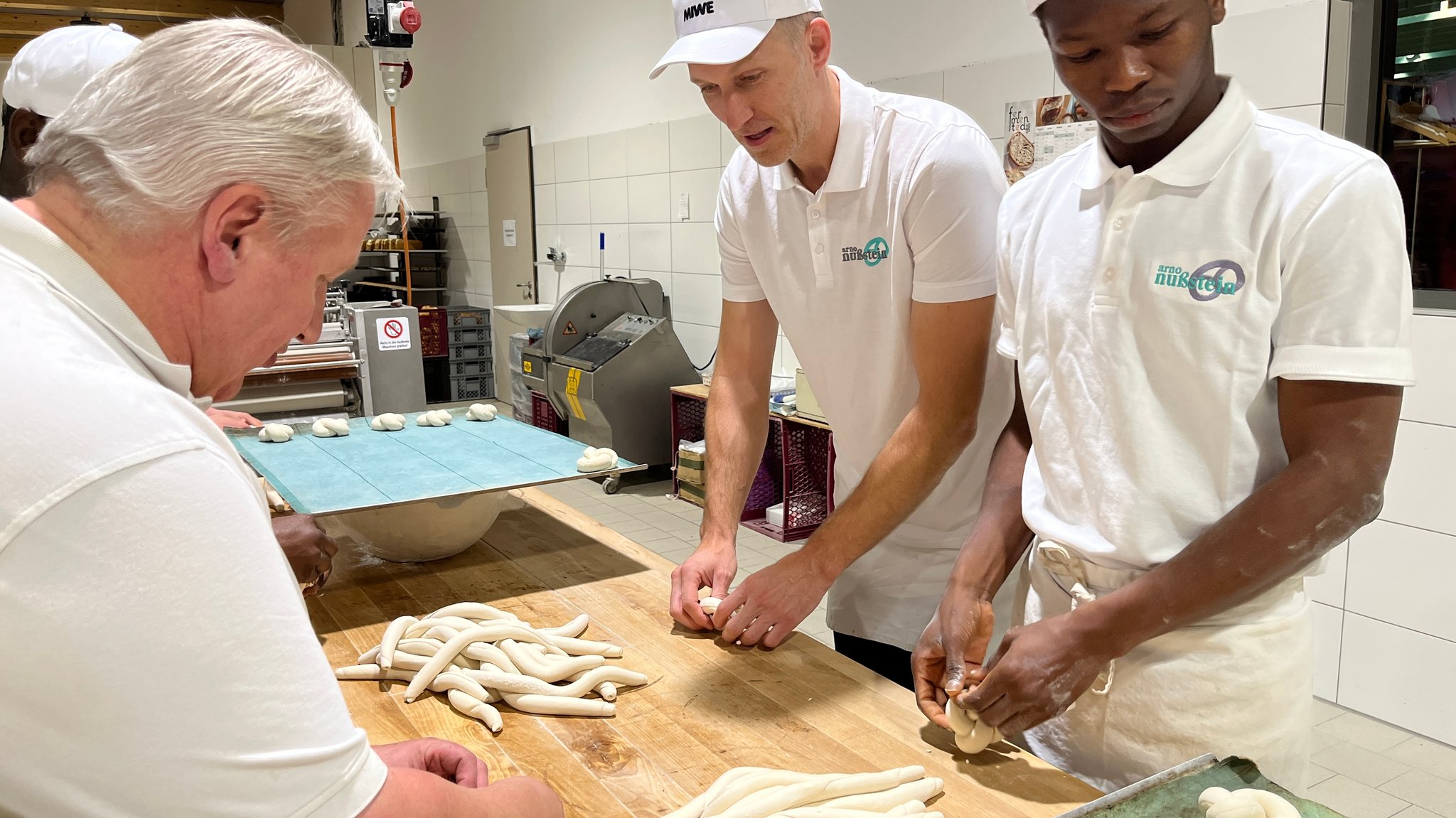 Der Vorstand der Bundesagentur für Arbeit bäckt als Praktikant mit zwei Bäckern Laugenzöpfe in einer Backstube. | Bild: BR/Margit Ringer Der Vorstand der Bundesagentur für Arbeit bäckt als Praktikant mit zwei Bäckern Laugenzöpfe in einer Backstube.