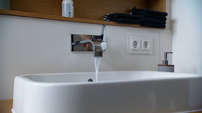 Wasser fließt aus dem Wasserhahn ins Waschbecken.
