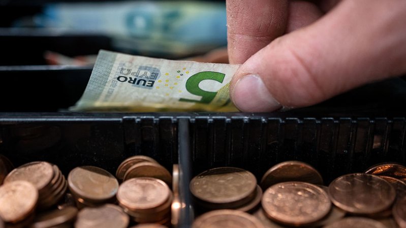 Die Inflation sinkt zum Jahresbeginn deutlich ab. Ein Mann nimmt einen 5-Euro-Schein aus einer Kasse. (Symbolbild) 