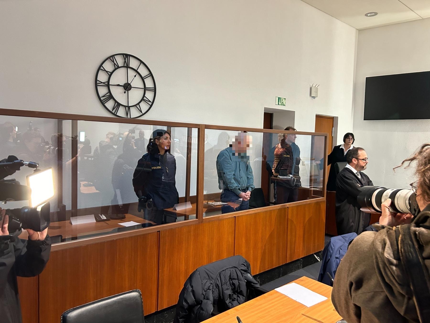 Der Angeklagte steht zwischen einem Polizeibeamten und einer Polizeibeamtin im Landgericht Hof. 