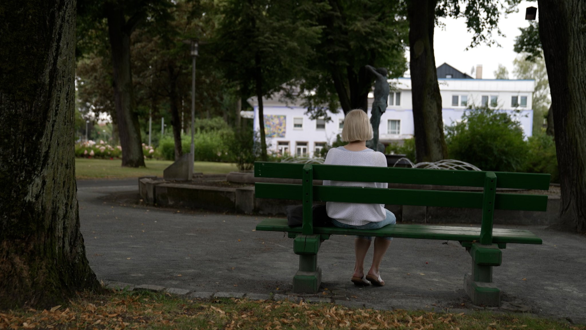 Eine Frau sitzt auf einer Bank vor dem Gebäude eines Reha-Zentrums.