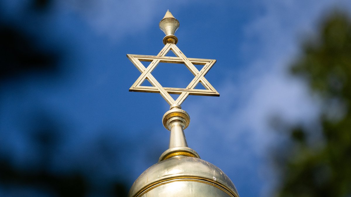In der Mitte sieht man die goldene Kuppel einer Synagoge mit einem Davidstern auf der Spitze. Im Hintergrund sieht man Bäume und den Himmel.