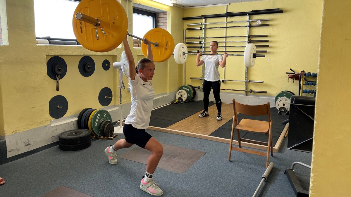 Zwei Mädchen trainieren mit ,Langhanteln in einem Trainingsraum Gewichtheben.