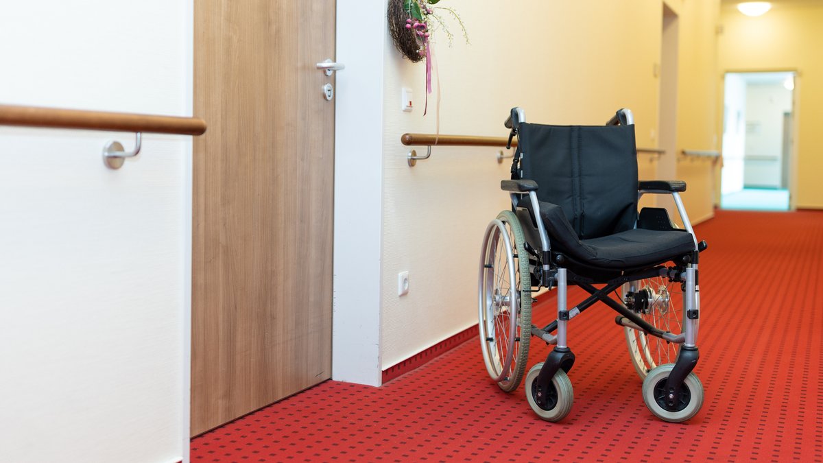 Auf einem Flur in einem Altenheim steht ein Rollstuhl vor der Zimmertüre