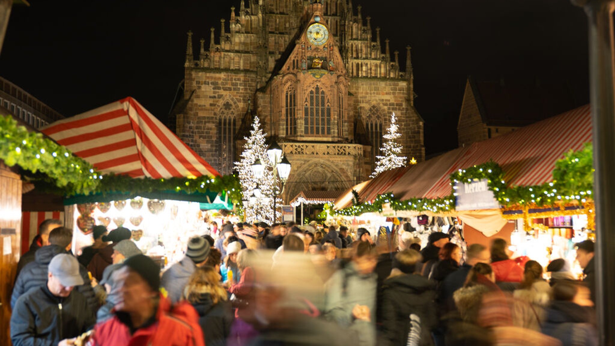 Nürnberger Christkindlesmarkt mit der beleuchteten Westfassade der Frauenkirche im Hintergrund.