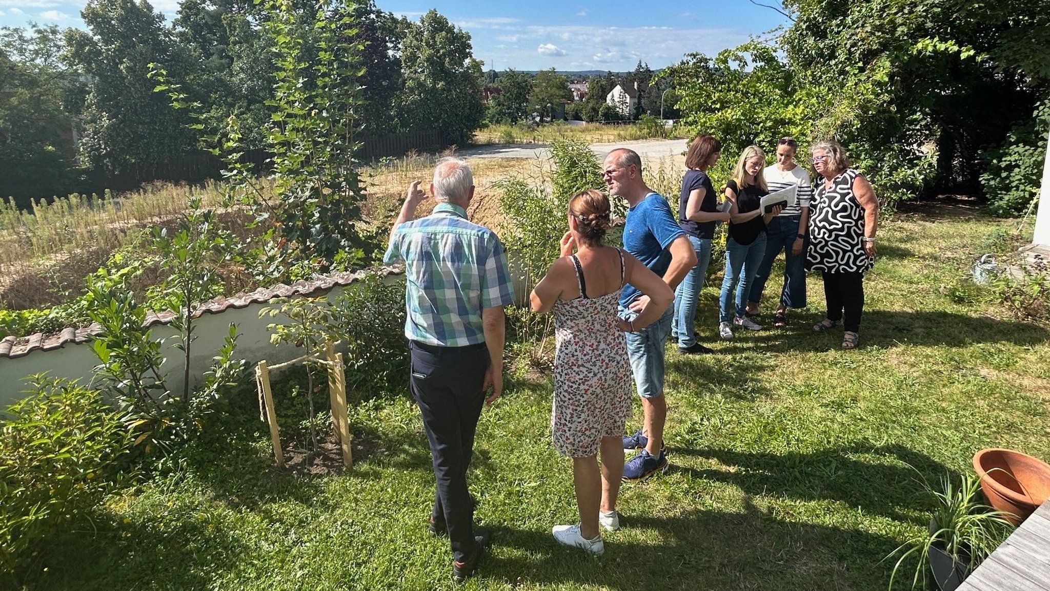 Menschen stehen auf einem Grundstück inmitten von Bäumen und Häusern.