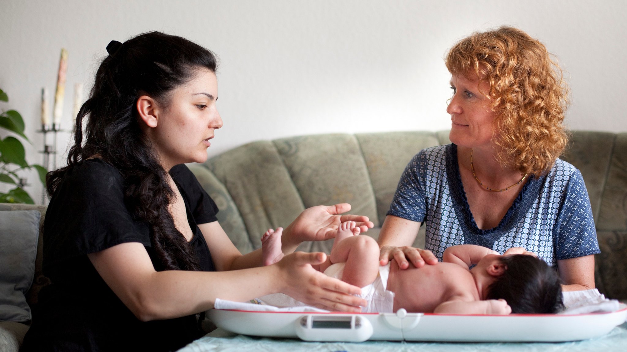 Eine Kinderkrankenschwester besucht eine Mutter und wiegt mit ihr das neugeborene Kind.