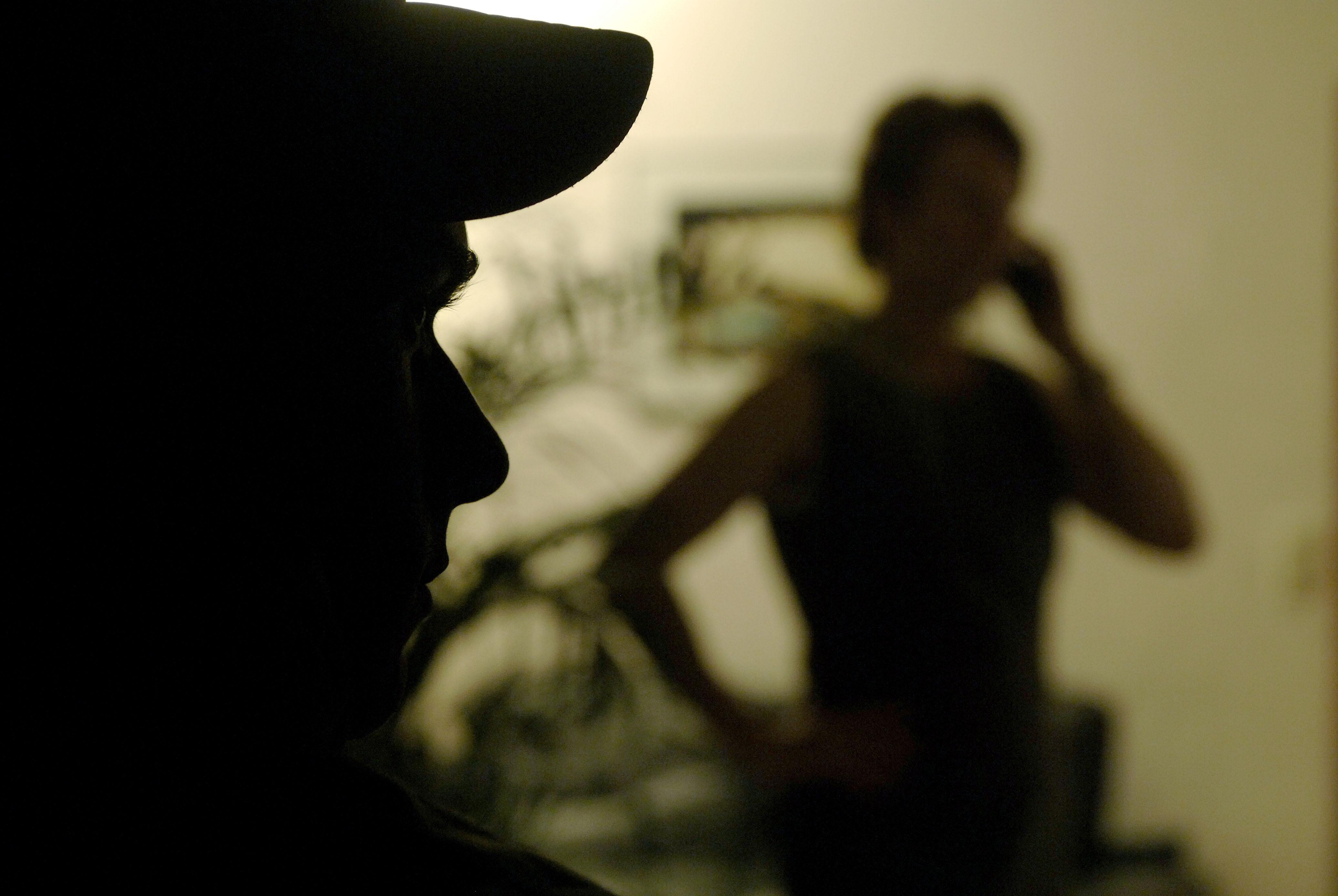 Eine im Schatten stehende, telefonierende Frau wird von einem Mann beobachtet.