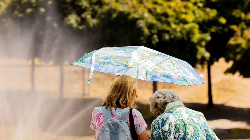 Zwei Frauen schützen am Rheinufer in der Altstadt mit einem Regenschirm vor der Sonne.