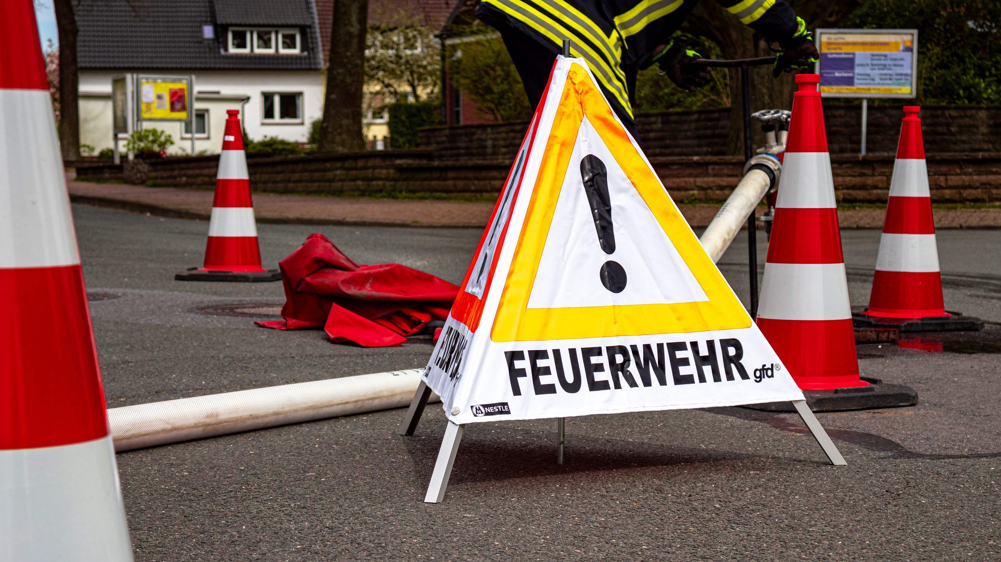 Ein Absperrdreieck mit der der Aufschrift "Feuerwehr" und mehrere Pylonen stehen auf einer Straße.