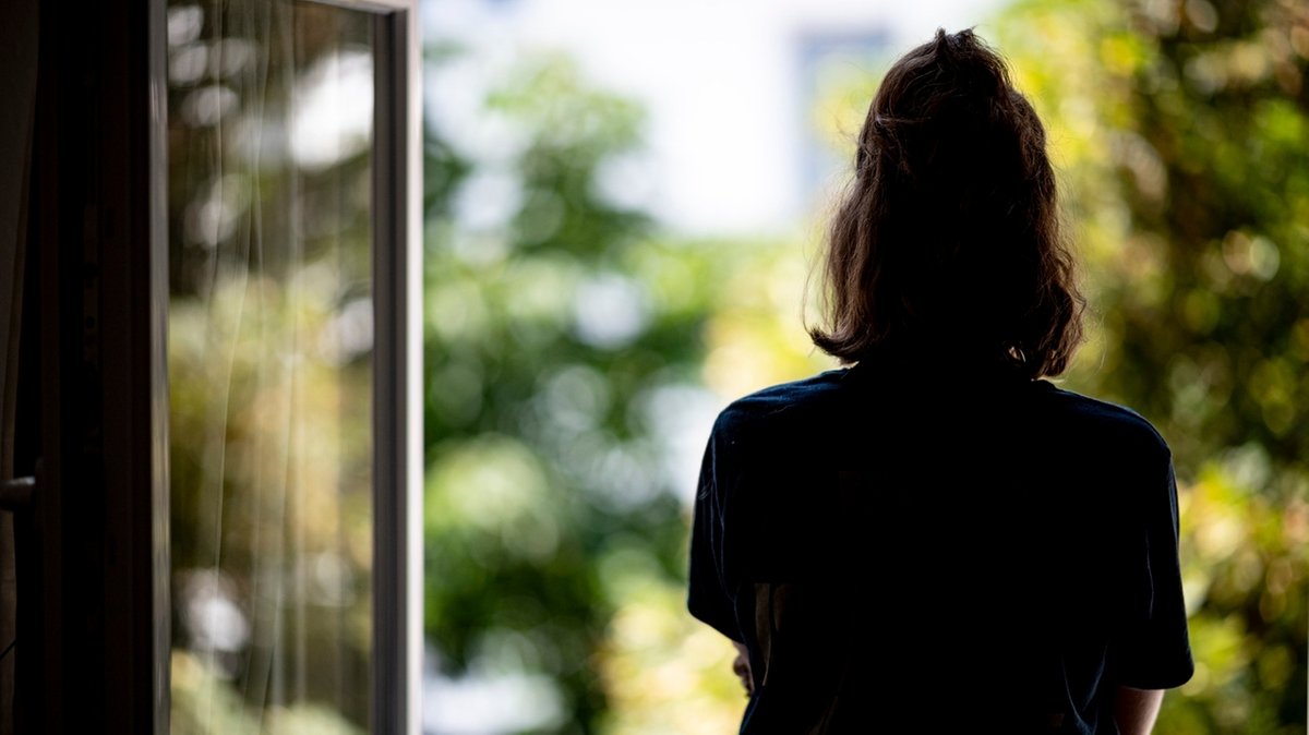 ILLUSTRATION - Eine Frau steht in ihrer Wohnung an einem Fenster. (gestellte Szene)
