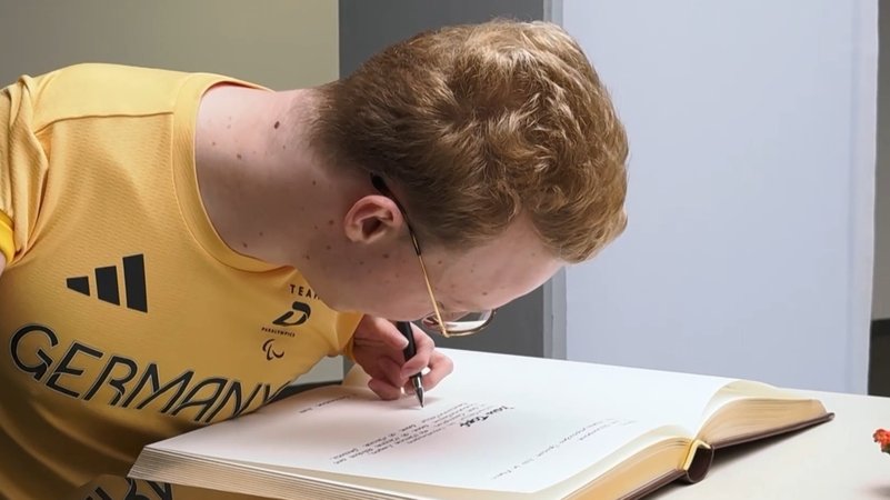 Ein Mann im gelben Trikot schreibt in ein Buch. | Bild: BR Ein Mann im gelben Trikot schreibt in ein Buch.