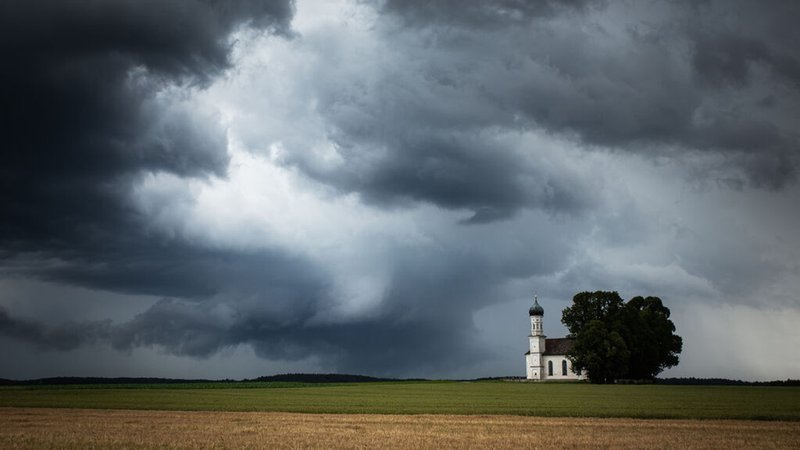 Dunkle Gewitterwolken hinter einer Kirche auf dem Land. | Bild: stock.adobe.com/natur-motive Dunkle Gewitterwolken hinter einer Kirche auf dem Land.