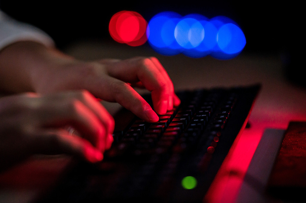 Hände tippen auf einer Tastatur, alles ist in rötliches Licht getaucht