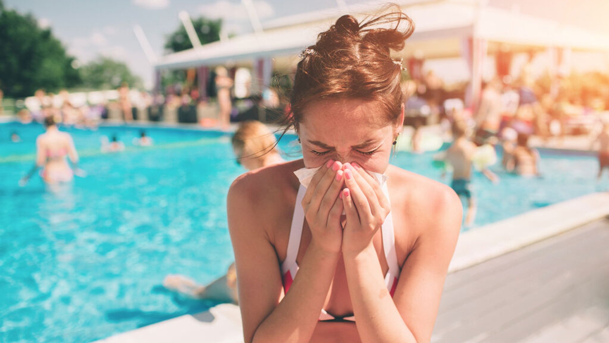 Eine Frau sitzt in einem Schwimmbad und schneuzt in ein Taschentuch.