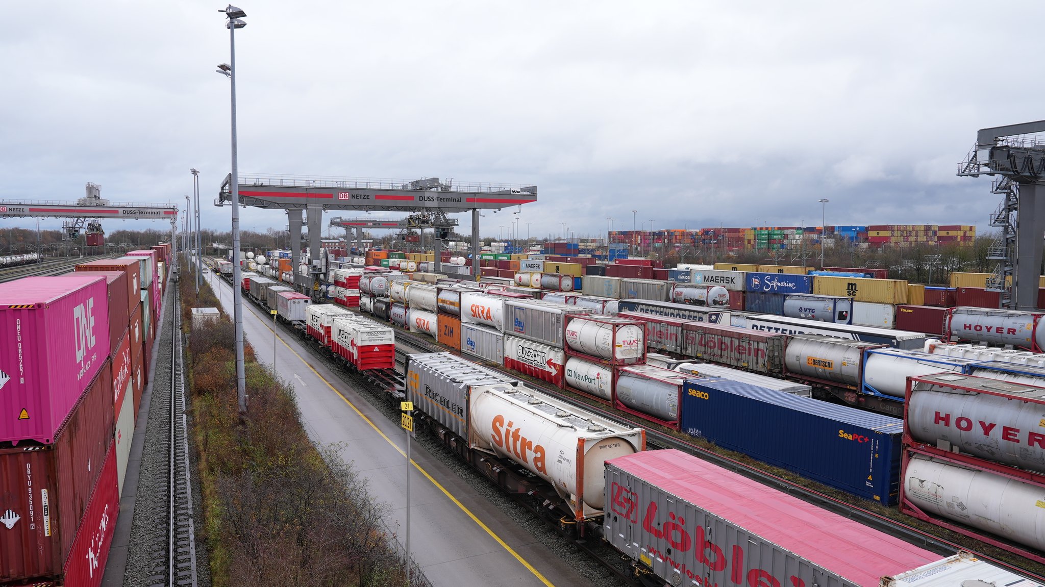 Foto: Totale des Bahnhofs, in mehreren Reihen stapeln sich Container, Züge stehen auf Gleisen und darüber arbeiten mehrere große Kräne