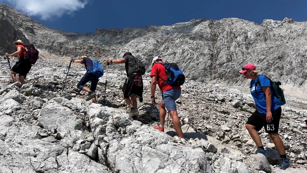 Fünf Menschen in Sportkleidung gehen mit Wanderstecken einen felsigen Weg nach oben, aufs Zugspitzplatt.