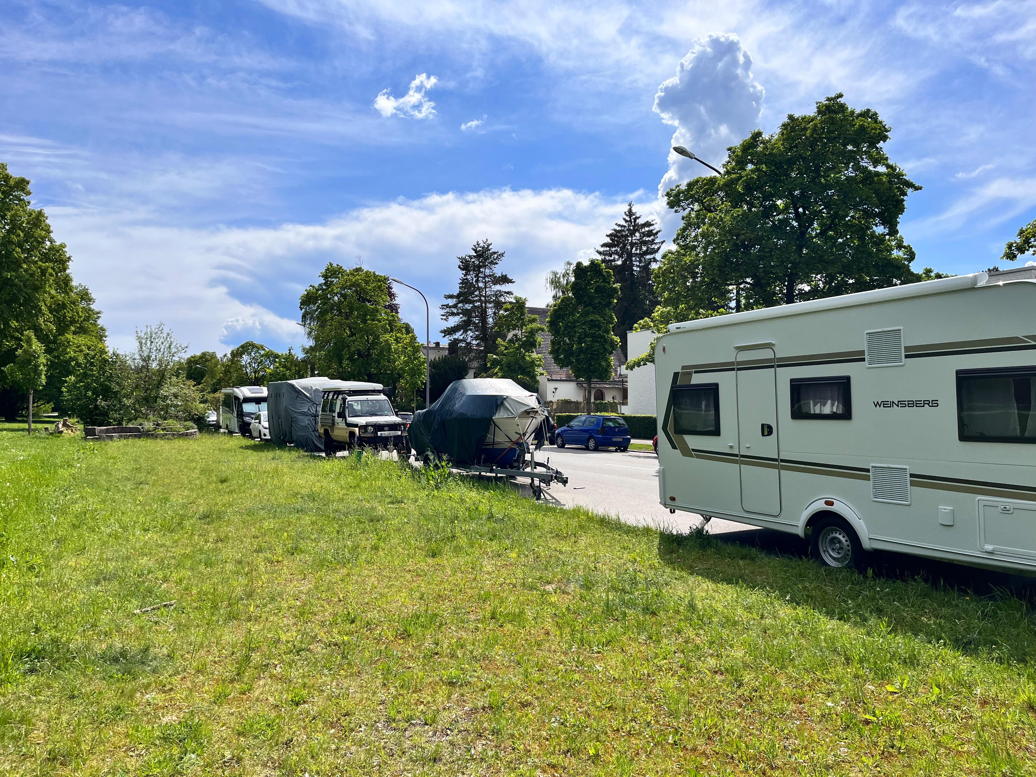Straße am Waldfriedhof in München mit vielen abgestellten Booten, Wohnwagen und Anhängern. 