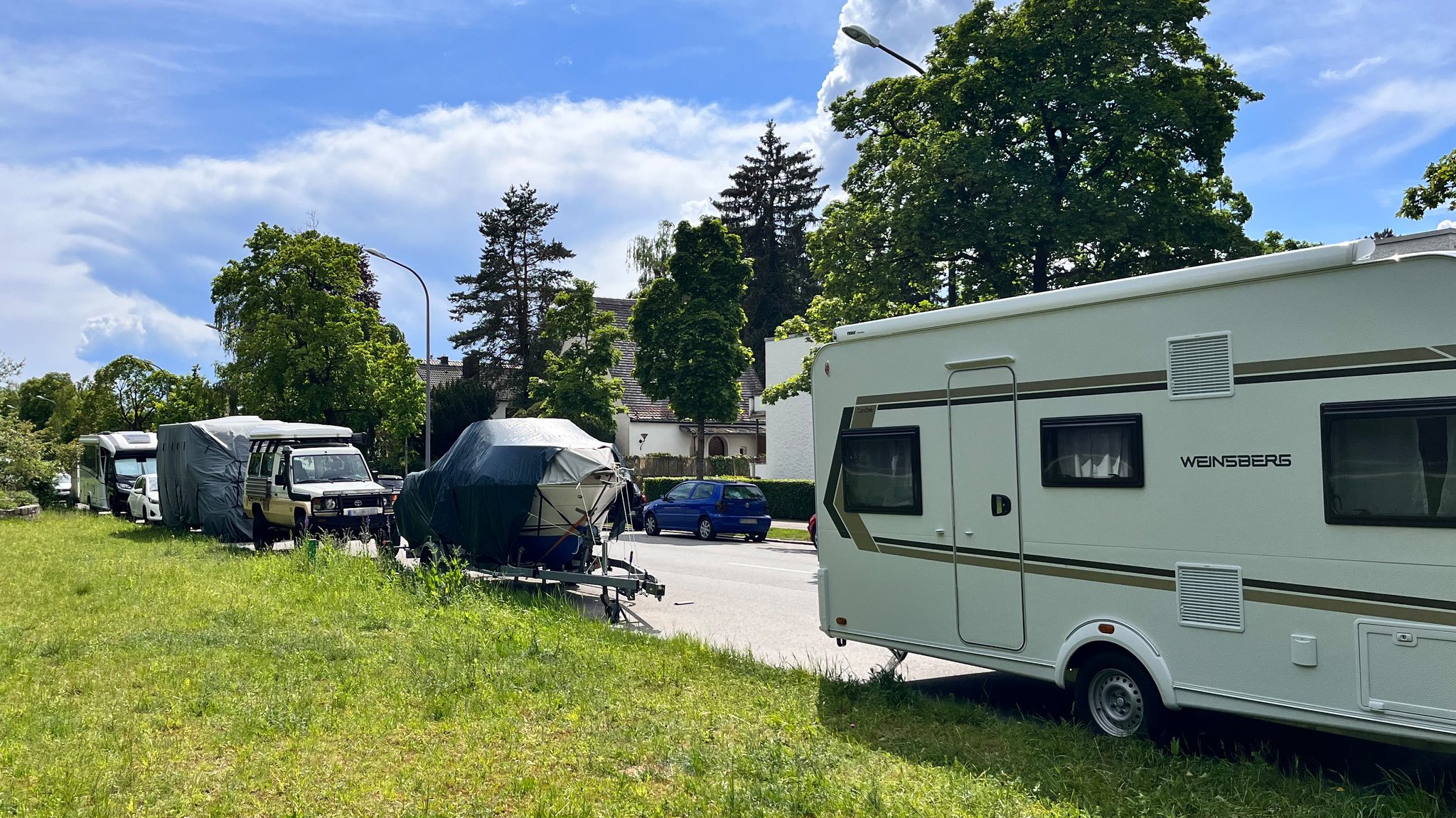 Straße am Waldfriedhof in München mit vielen abgestellten Booten, Wohnwagen und Anhängern. 