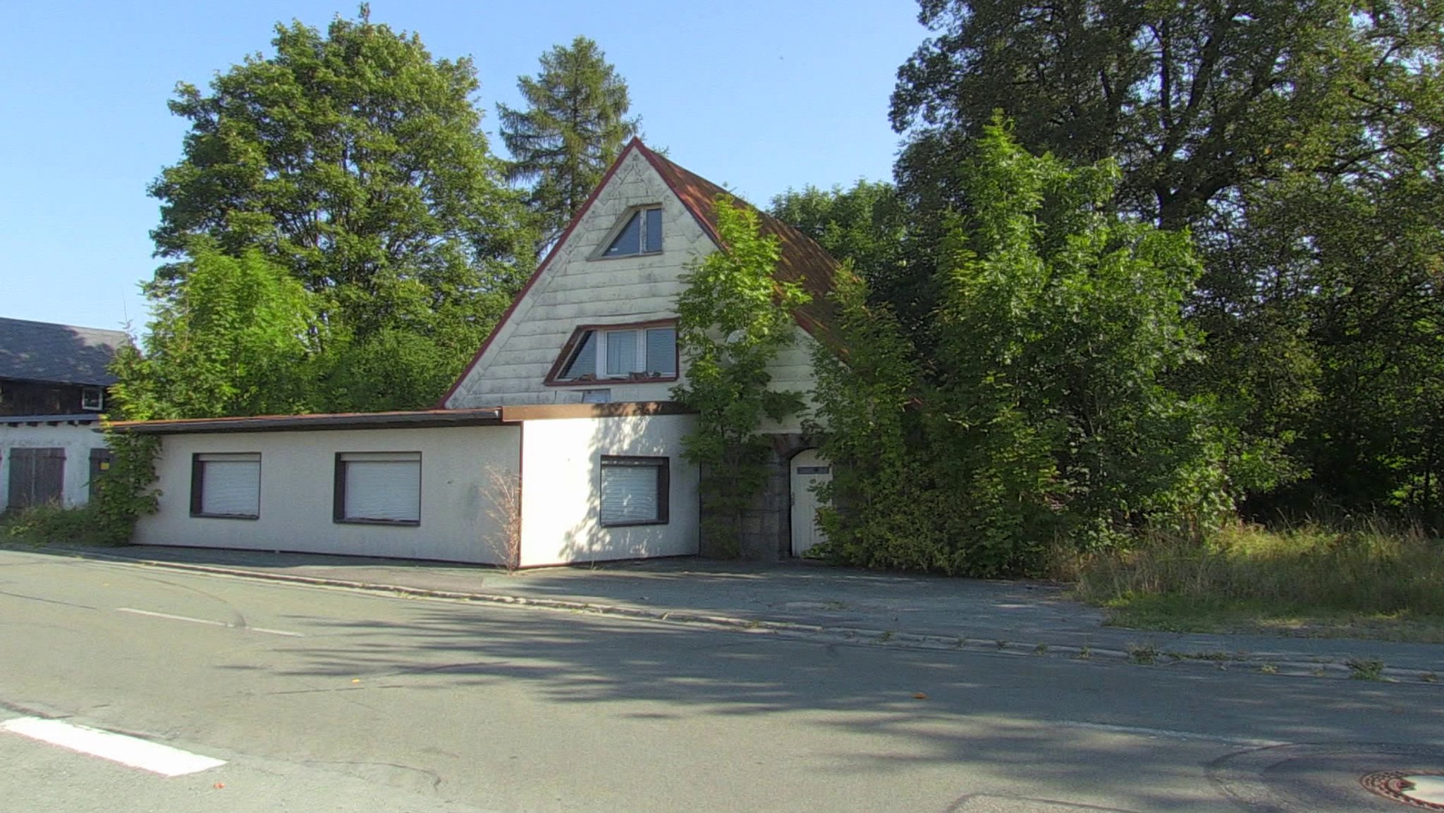 Ein Haus mit Vorbau, von vielen Bäumen umwachsen.