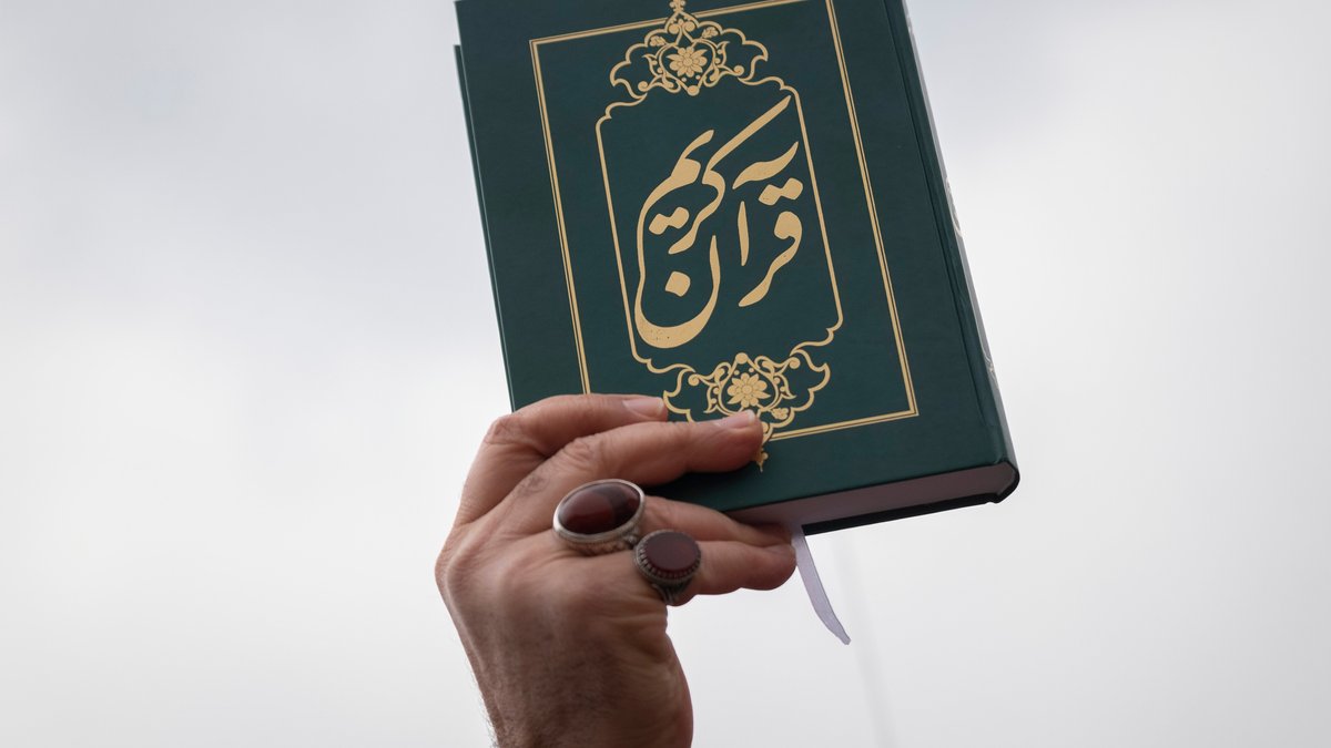 Eine Hand hält ein Exemplar des Korans in die Höhe (Symbolbild)