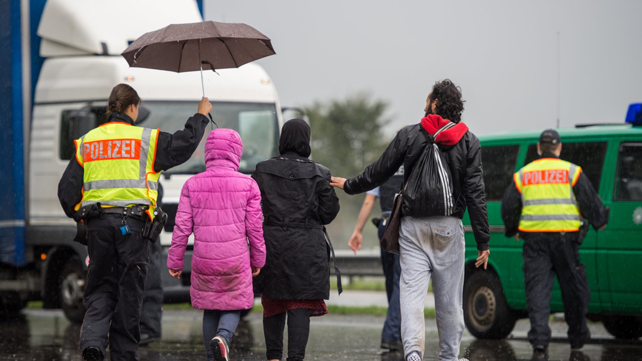 Eine syrische Familie wird von einer Polizistin zu einem Auto begleitet.