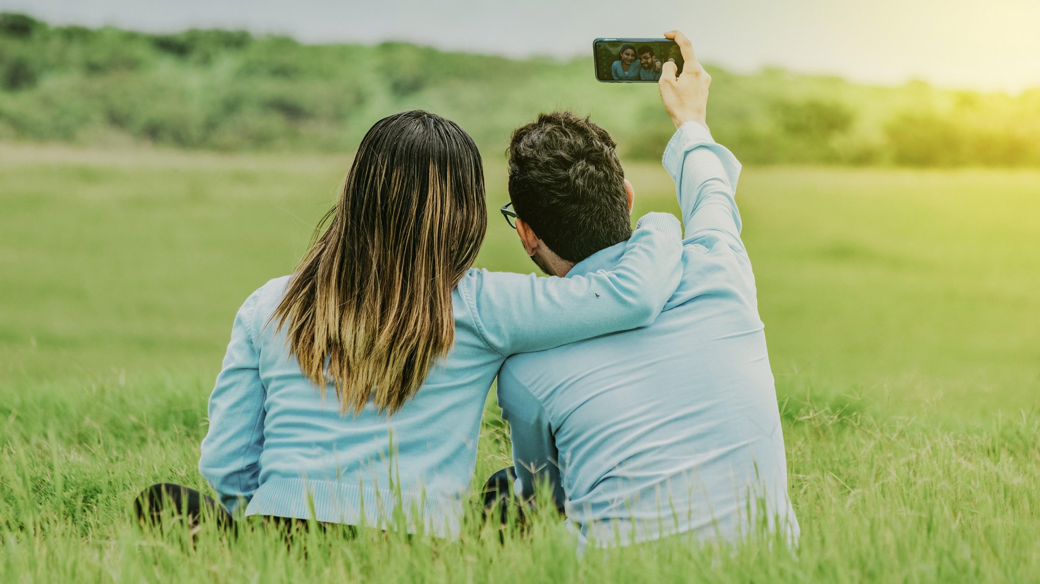  Junges glückliches Paar nimmt ein Selfie im Feld sitzend auf