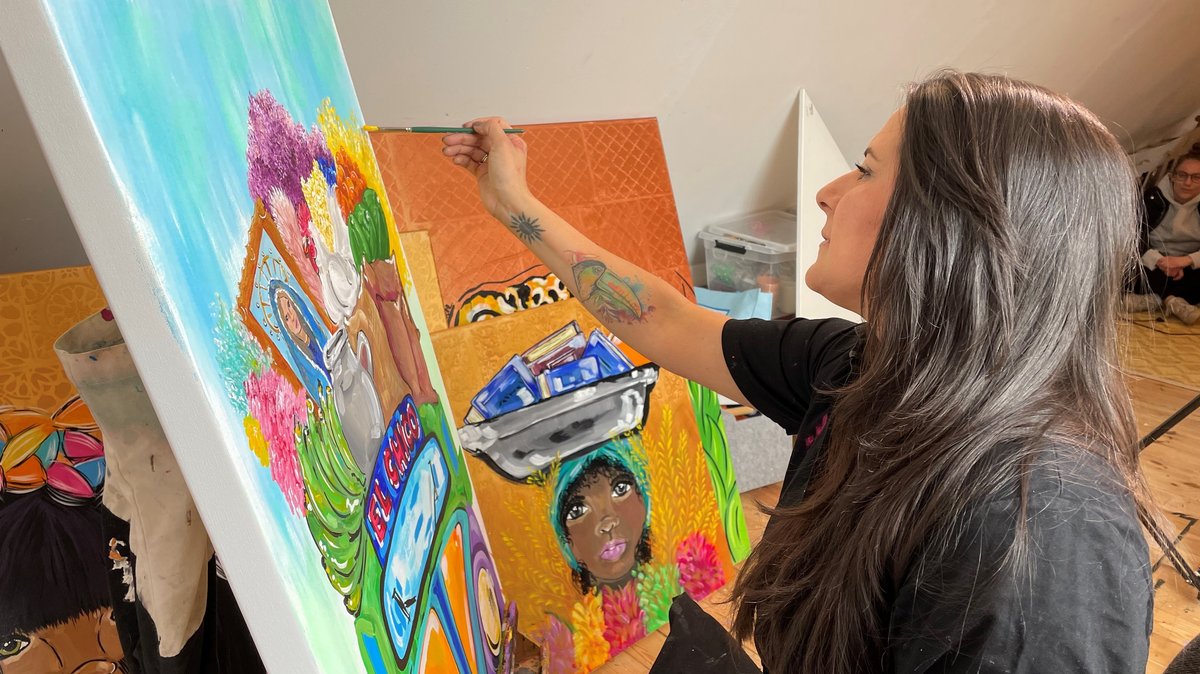 Die Künstlerin Liliana Martinez sitzt vor einer Staffelei und malt ein farbenfrohes Bild.