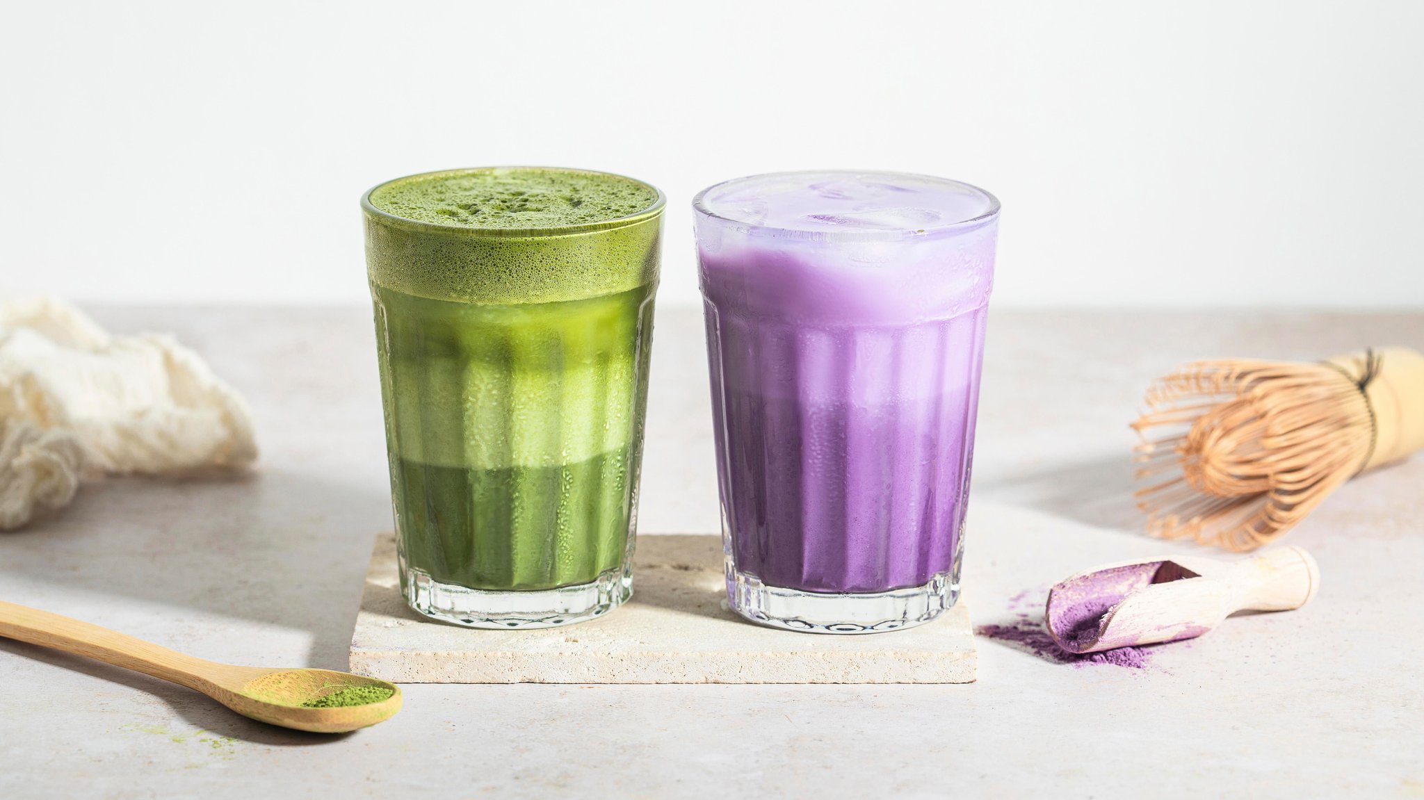 Ein grüner Matcha Latte und ein violetter Ube Latte im Glas.