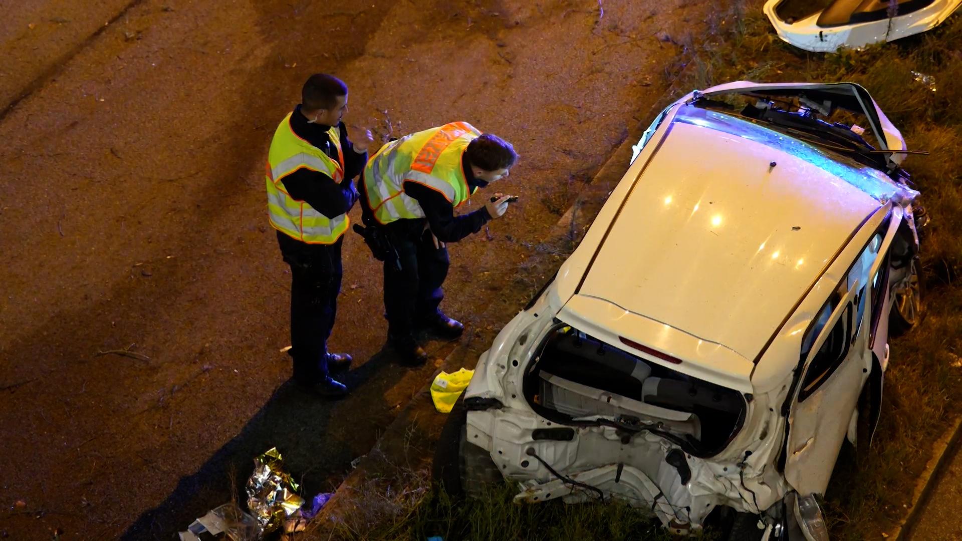 Zwei Polizisten in Warnwesten inspizieren ein verunfalltes Auto