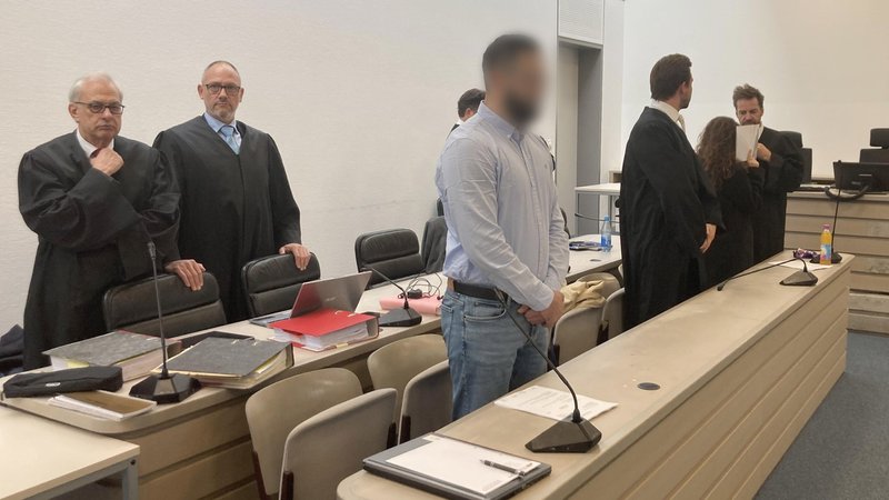 Anwälte stehen in ihren Roben im Gerichtssaal, vor ihnen liegen dicke Aktenordner. Das Gesicht des jungen Mannes in der ersten Reihe ist verpixelt. Eine junge Frau hält sich einen Block vors Gesicht. Sie sitzen weit auseinander. | Bild: picture alliance/dpa | Sabine Dobel Anwälte stehen in ihren Roben im Gerichtssaal, vor ihnen liegen dicke Aktenordner. Das Gesicht des jungen Mannes in der ersten Reihe ist verpixelt. Eine junge Frau hält sich einen Block vors Gesicht. Sie sitzen weit auseinander.