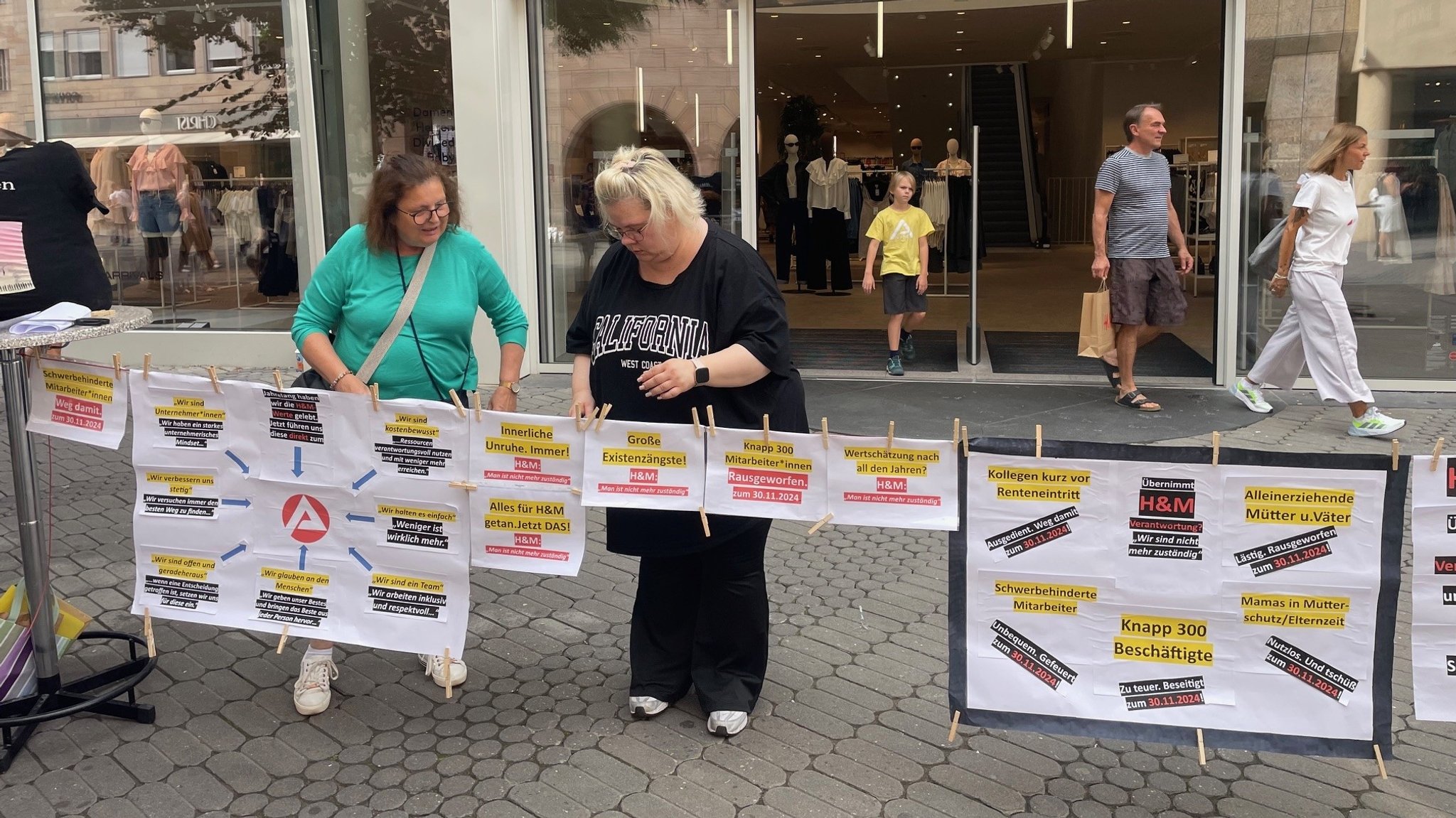 Zwei Frauen hängen beschriebene Papierblätter an einer Wäscheleine in der Nürnberger Innenstadt auf