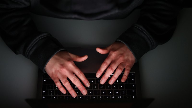 Symboldbild: Hände über einer Computertastatur. Der Mann ist schwarz gekleidet.