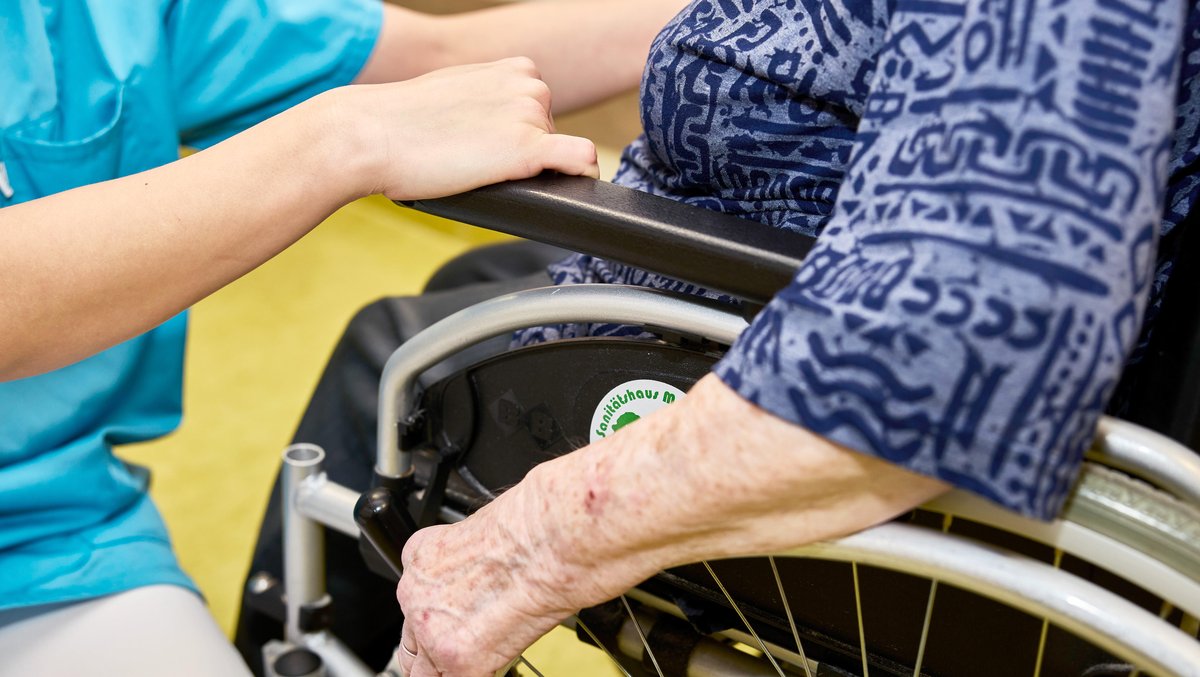 Pfllegekraft und Bewohnerin im Rollstuhl auf dem Flur in einem Pflegeheim