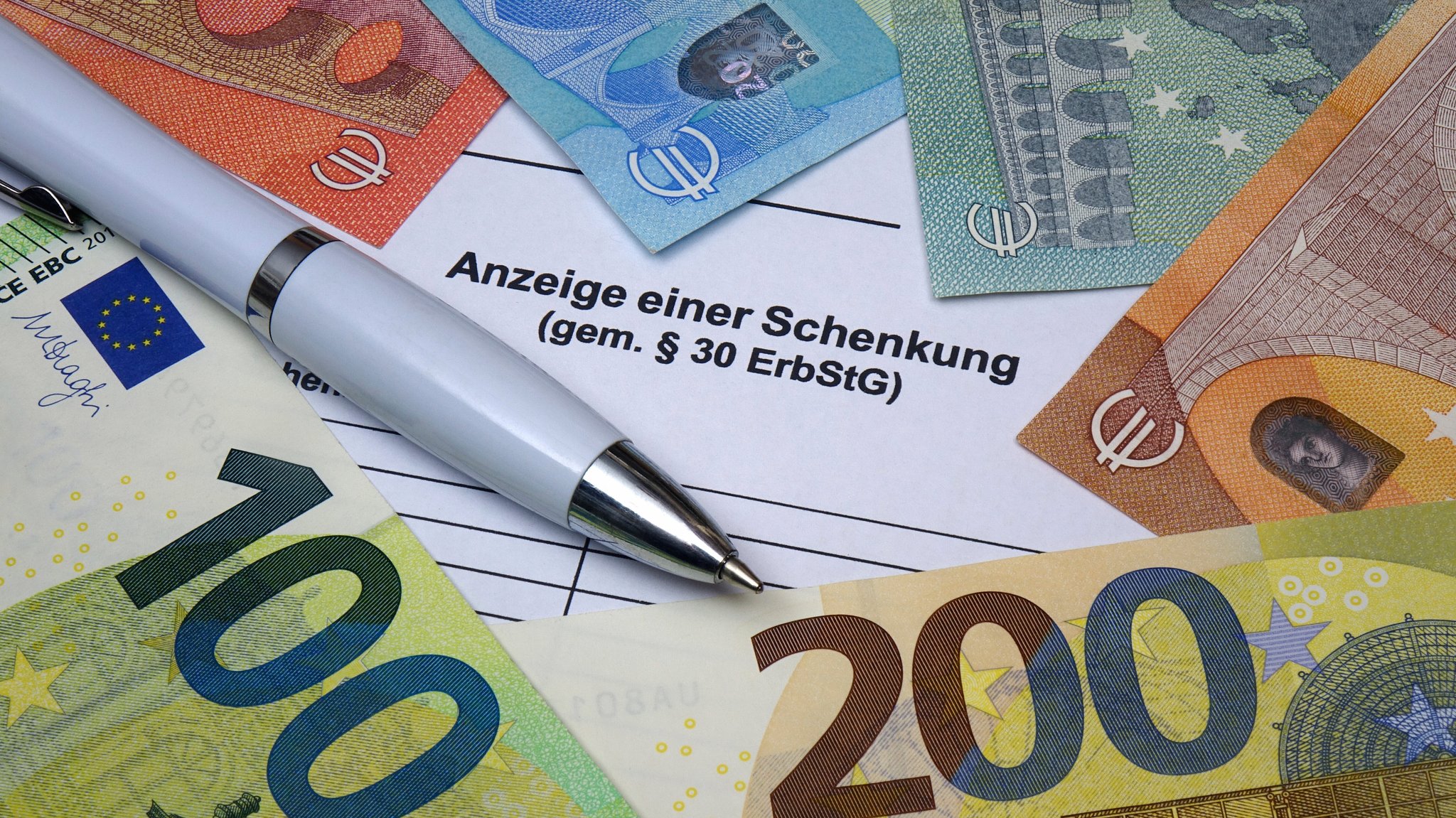 Auf der Anzeige einer Schenkung liegt ein Kugelschreiber, darumherum Geldscheine.