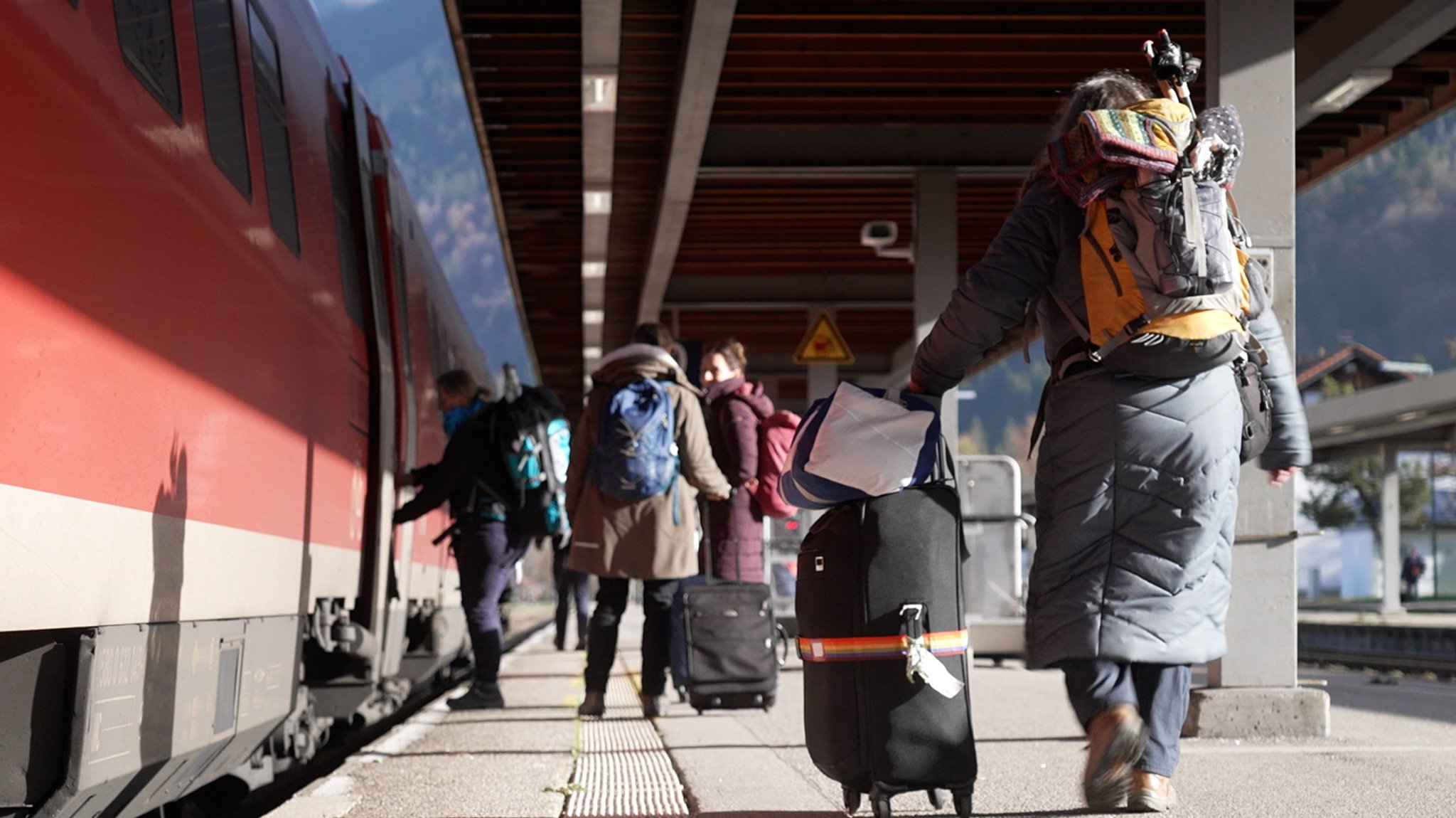 Mehrere Menschen mit Koffern und Rucksäcken steigen am Bahnhof in Oberstdorf in einen roten Regionalzug