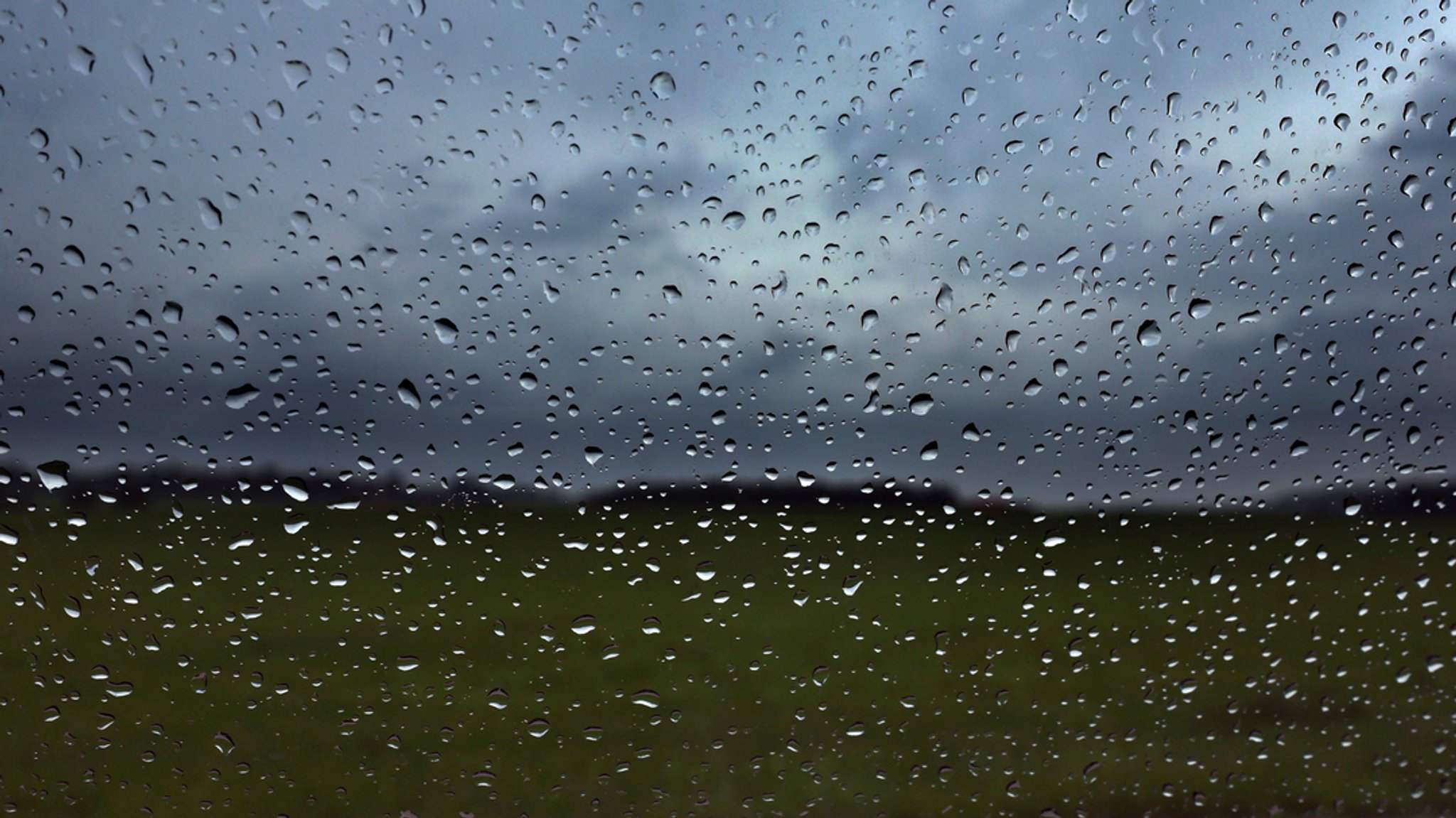 Eine Autoscheibe ist vor dunklen Wolken mit Regentropfen bedeckt.