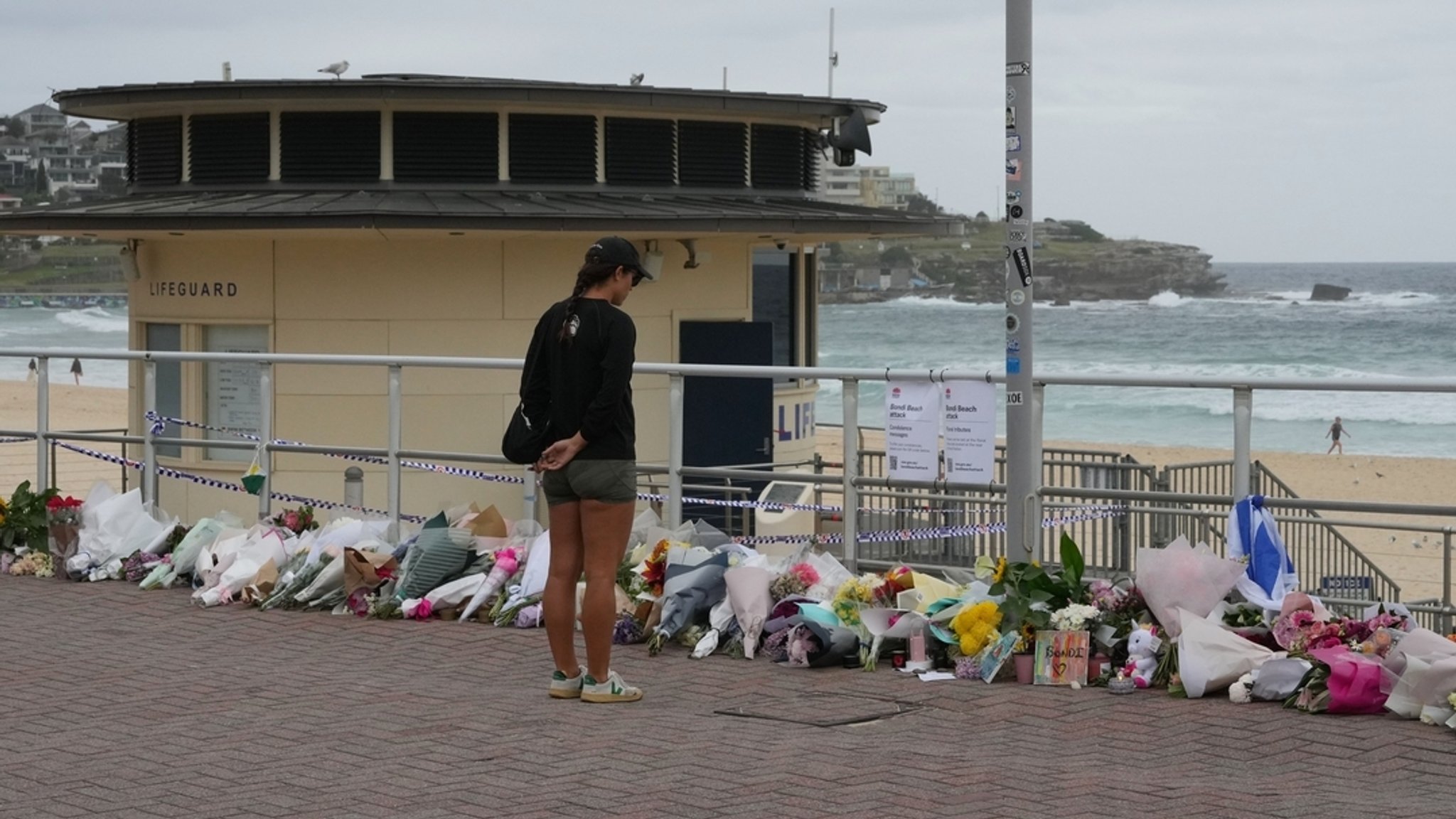 Eine Frau steht am Bondi Beach vor abgelegten Blumen in Gedenken an die Getöteten.