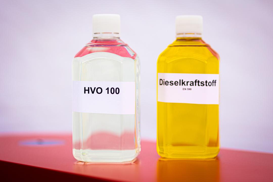 Eine Flasche mit dem Biokraftstoff HVO (Hydrotreated Vegetable Oil) und eine Flasche mit Dieselkraftstoff stehen bei einem Pressetermin auf einem Tisch.