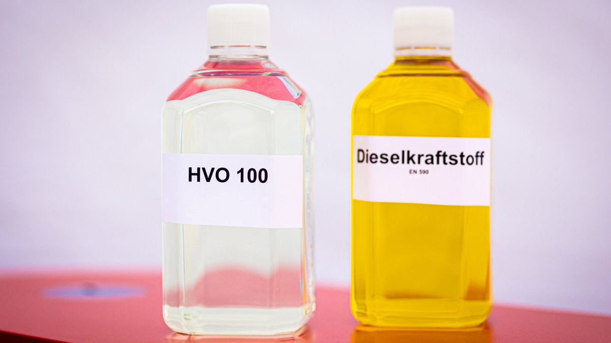 Eine Flasche mit dem Biokraftstoff HVO (Hydrotreated Vegetable Oil) und eine Flasche mit Dieselkraftstoff stehen bei einem Pressetermin auf einem Tisch.