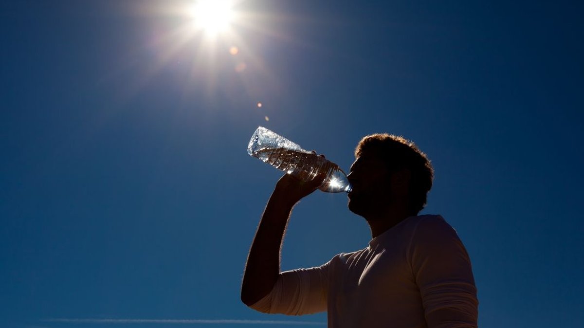Ein Mann trinkt aus einer Wasserflasche bei strahlender Sonne.