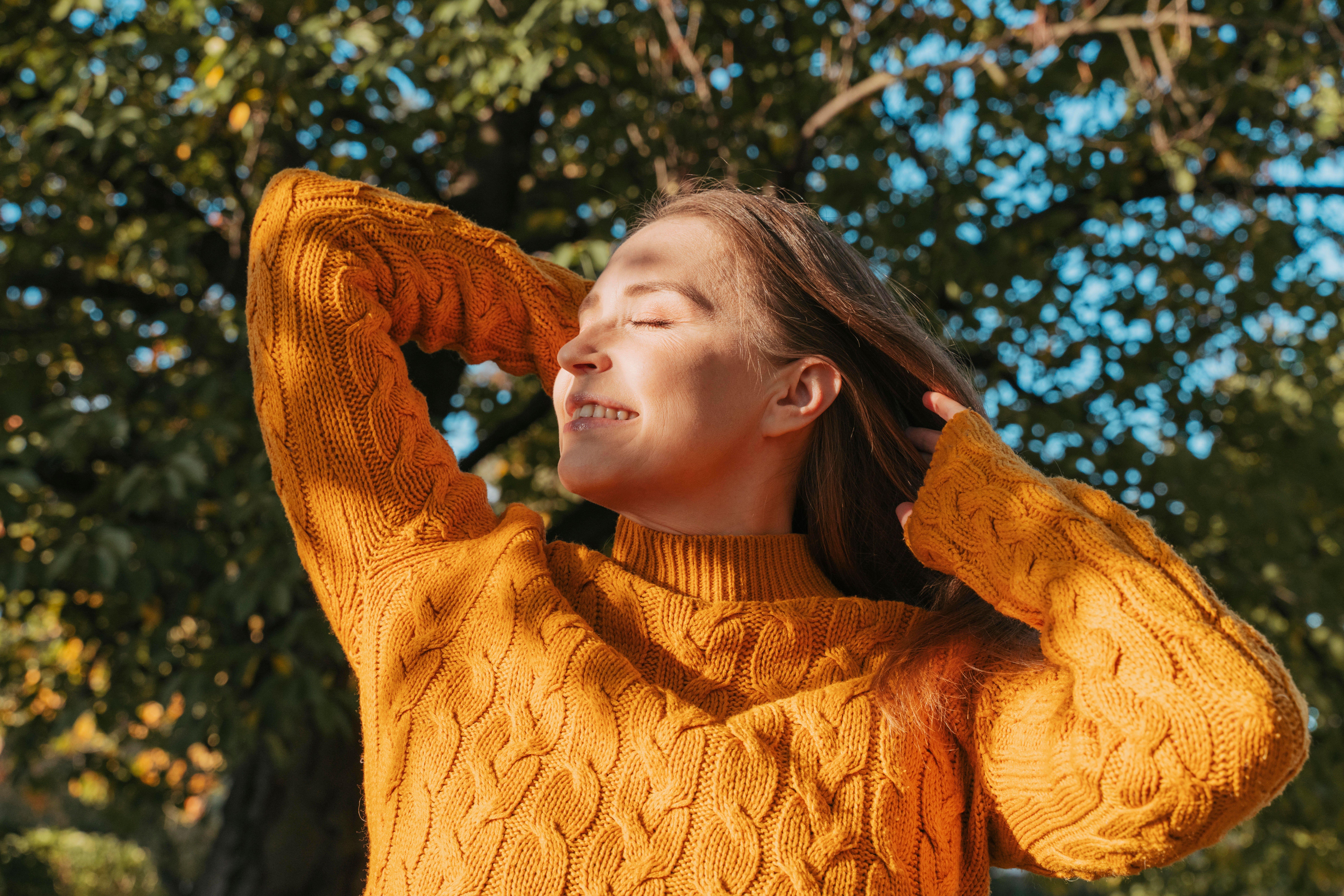 Eine Frau im orangen Pullover schaut genießerisch in die Herbstsonne
