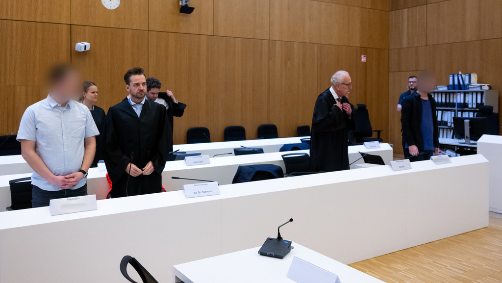 Die zwei wegen Mordes angeklagten Männer (l und r) stehen am 6. März vor Beginn der Verhandlung im Hochsicherheitsgerichtssaal vom Landgericht München II neben ihren Rechtsanwälten.