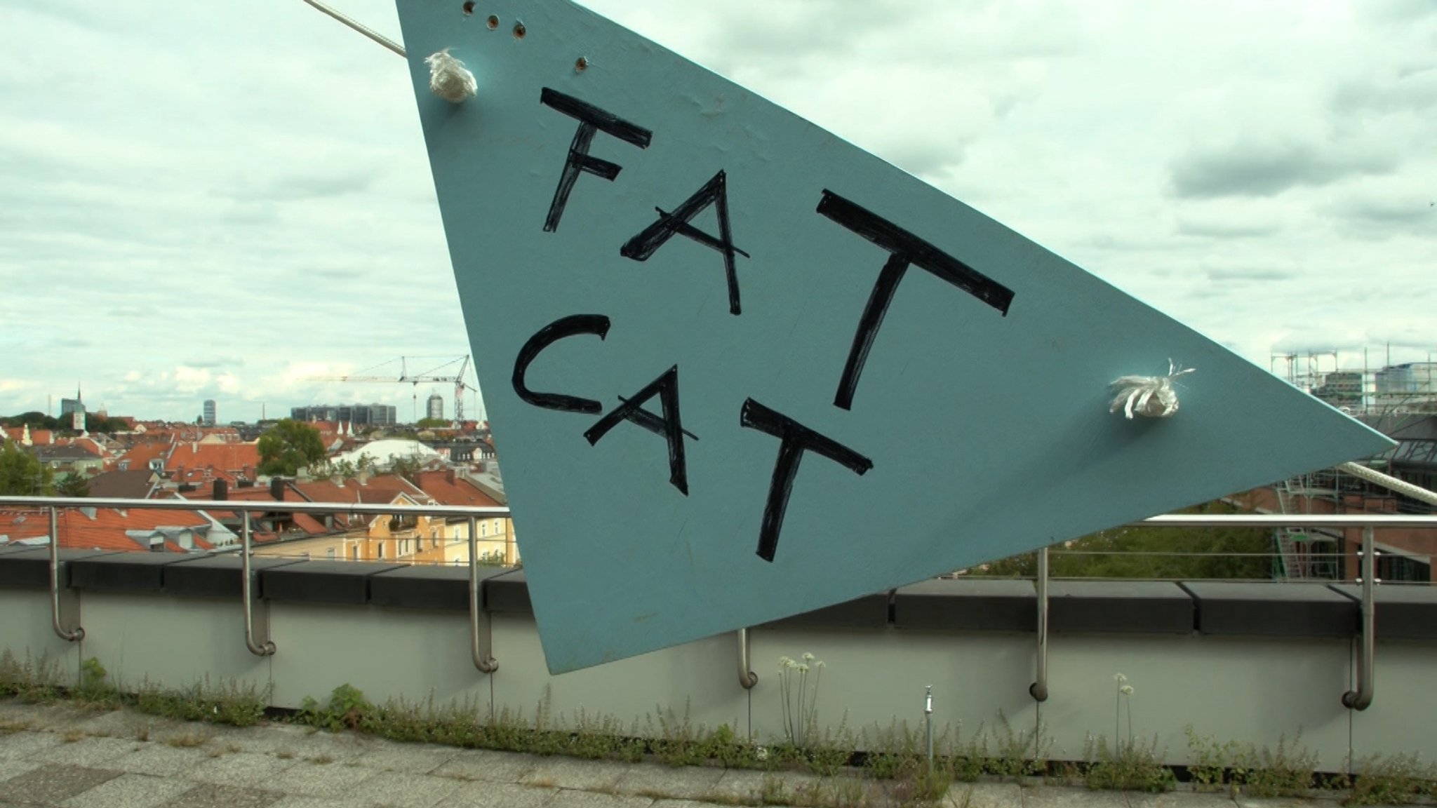 Fat Cat steht auf einem dreieckigen Schild auf dem Dach des Kulturzentrums in München. | Bild: BR24 Fat Cat steht auf einem dreieckigen Schild auf dem Dach des Kulturzentrums in München.