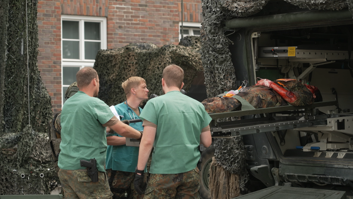 Soldaten schieben einen Verletzten auf einer Trage in einen Panzer. 